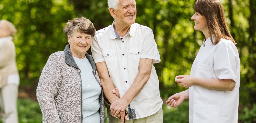 Elderly couple in a garden with a carer, all smiling